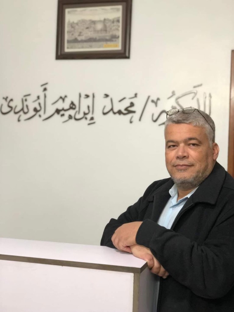 د. محمد إبراهيم أبو ندى في عيادته مع خط عربي لاسمه على الحائط